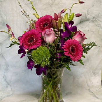 Pink gerberas, roses, and purple orchids in a clear glass vase