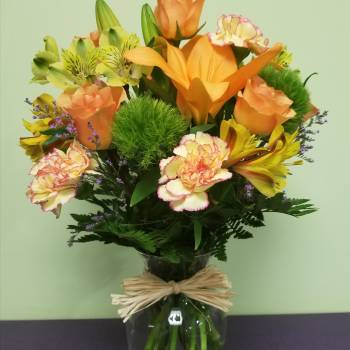 Orange and yellow mixed bouquet in a glass vase with a raffia bow