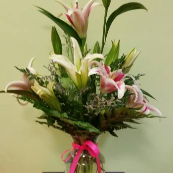 Bouquet of pink and white lilies in a glass vase with a pink ribbon