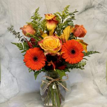 Bouquet of orange gerbera daisies and yellow-orange roses in a glass vase