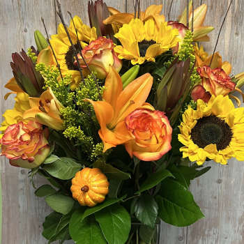 Bouquet of sunflowers, orange roses, and lilies in a glass vase