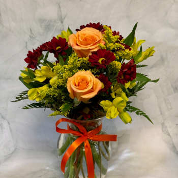 Bouquet of peach roses, red daisies, and yellow flowers in a glass vase
