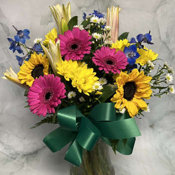 Bouquet of sunflowers, pink gerberas, and blue flowers in a glass vase