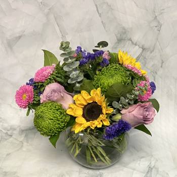 Mixed bouquet with sunflowers, pink roses, and green chrysanthemums in a glass vase