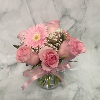 Pink roses and a gerbera daisy in a glass vase with a pink ribbon