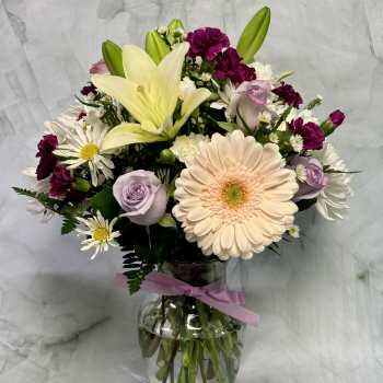 Mixed bouquet with lilies, roses, daisies, and carnations in a glass vase