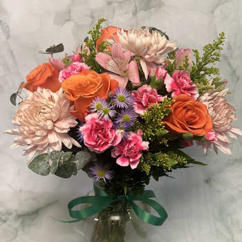 Mixed bouquet of orange roses, pink carnations, and pale chrysanthemums in a glass vase