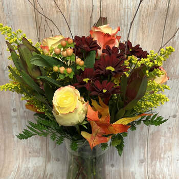 Bouquet of cream and orange roses with dark burgundy daisies in a glass vase