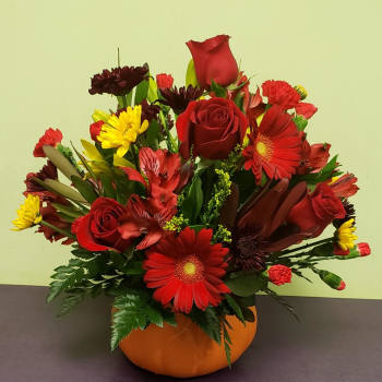 Red and yellow mixed flower arrangement in an orange pumpkin vase