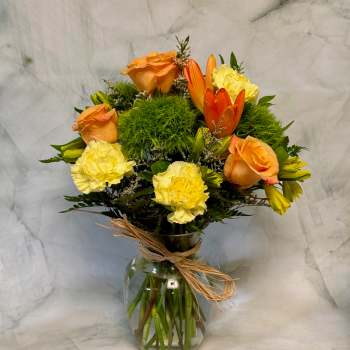 Orange roses and yellow carnations in a glass vase with raffia tie