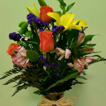 Mixed bouquet of lilies, roses, and purple filler flowers in a glass vase