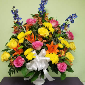 Colorful mixed flower arrangement in a white vase with a white bow