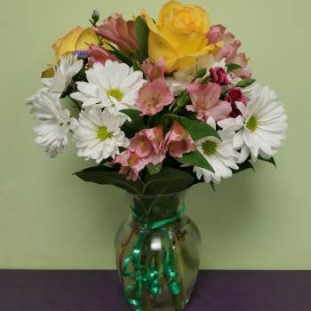 Bouquet of yellow roses, white daisies, and pink alstroemeria in a glass vase