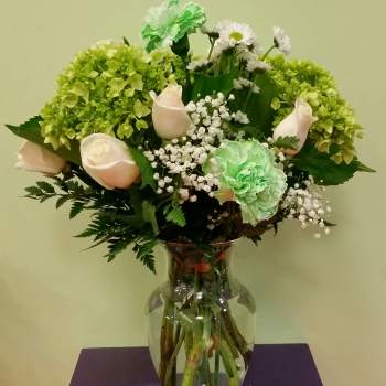 Bouquet of pale roses, green carnations, and white daisies in a glass vase