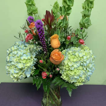 Mixed bouquet in a glass vase with hydrangeas, roses, and tall green spikes
