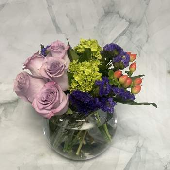 Lavender roses with purple and lime-green flowers in a glass vase