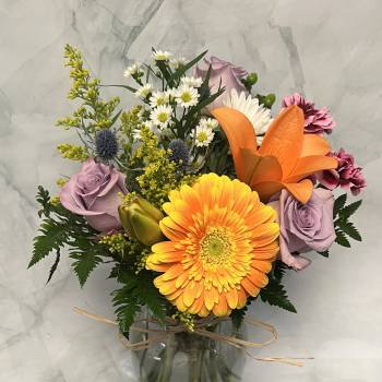 Mixed bouquet with orange gerbera, lavender roses, and lilies in a glass vase