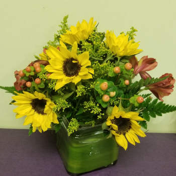 Sunflower arrangement in a green glass vase with berries and greenery