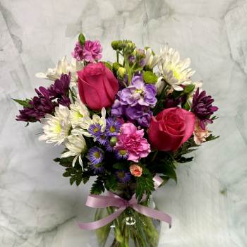 Mixed bouquet of pink roses, purple flowers, and white daisies in a glass vase
