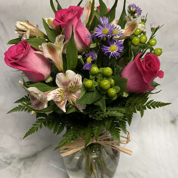 Pink roses and purple daisies arranged in a glass vase