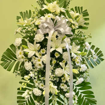 White floral standing spray with lilies, daisies, and a ribbon bow
