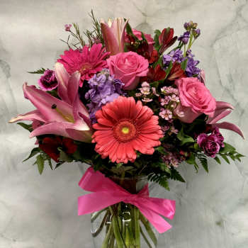 Pink and purple mixed bouquet in a glass vase with a bright ribbon