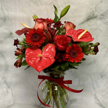 Red floral bouquet with anthuriums, roses, and gerbera daisies in a glass vase