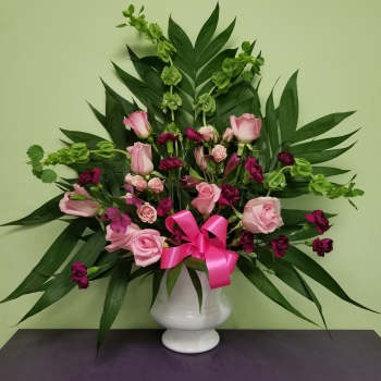 Pink roses and magenta flowers in a white vase with a pink ribbon