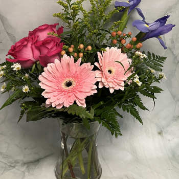 Pink roses and gerbera daisies in a clear glass vase with purple irises