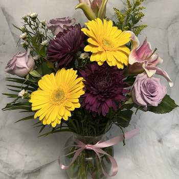 Bouquet of yellow gerbera daisies, purple chrysanthemums, and lavender roses in a glass vase