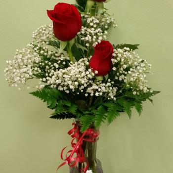 Three red roses in a clear glass vase with white baby's breath
