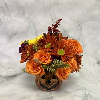 Orange roses and autumn-toned daisies in a pumpkin-shaped vase