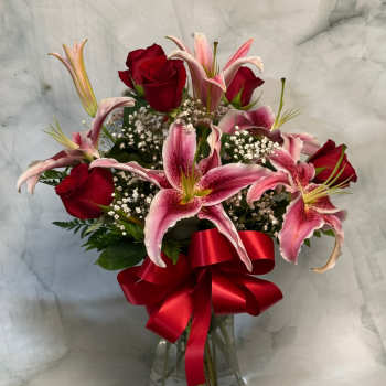 Red roses and pink lilies in a glass vase with a red ribbon