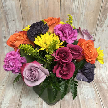 Colorful bouquet of roses, carnations, and yellow daisies in a glass vase