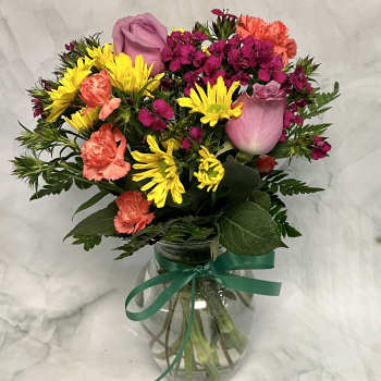 Mixed bouquet of pink roses, yellow daisies, and coral carnations in a glass vase