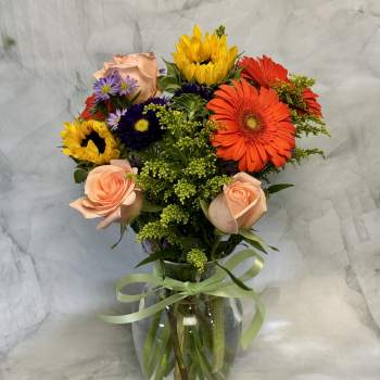 Mixed bouquet of roses, gerbera daisies, and sunflowers in a glass vase