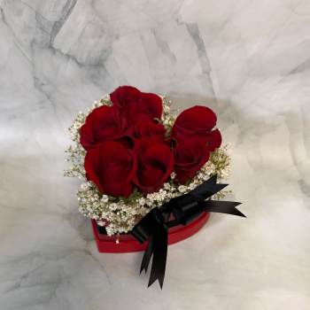 Red roses arranged in a heart-shaped box with white filler flowers and a black ribbon