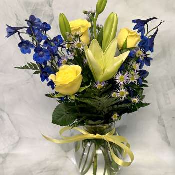 Yellow roses and blue delphinium in a glass vase with a ribbon.