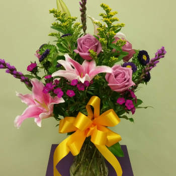 Pink roses and lilies in a glass vase with a yellow ribbon