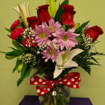 Bouquet of red roses, pink daisies, and white lilies in a glass vase