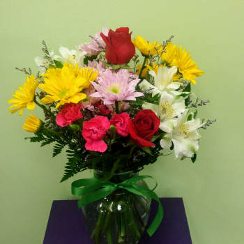 Mixed bouquet of roses, daisies, carnations, and alstroemeria in a glass vase
