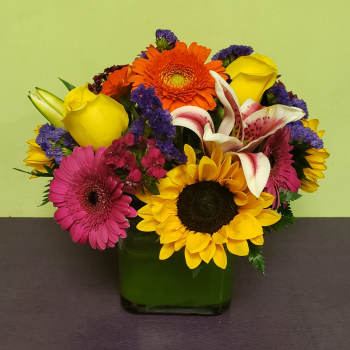 Colorful mixed bouquet in a green glass vase with sunflowers and roses