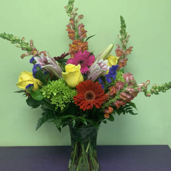 Mixed bouquet with roses, gerbera daisies, lilies, and snapdragons in a glass vase