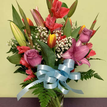 Mixed bouquet of tulips, roses, and lilies in a glass vase with a blue ribbon