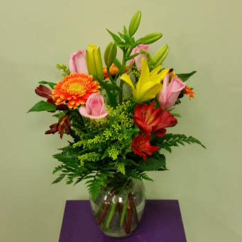 Mixed bouquet of lilies, roses, and gerbera daisies in a glass vase