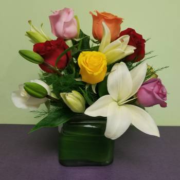 Mixed roses and lilies arranged in a green glass vase