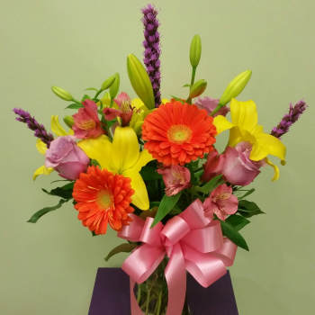 Bouquet of yellow lilies, orange gerberas, and pink roses in a glass vase