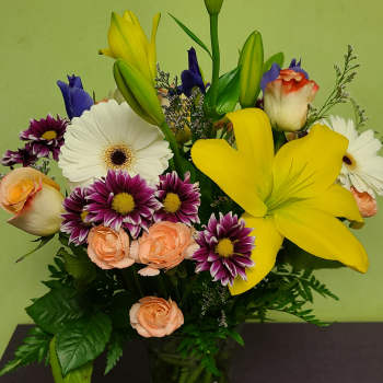 Mixed bouquet with yellow lilies, white gerberas, and peach roses in a glass vase
