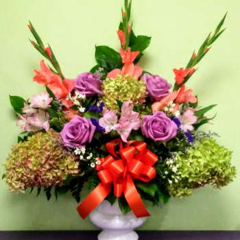 Colorful mixed flower arrangement in a white vase with a red bow