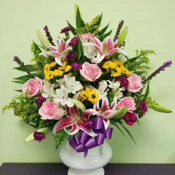 Pink roses and lilies in a white vase with a purple ribbon
